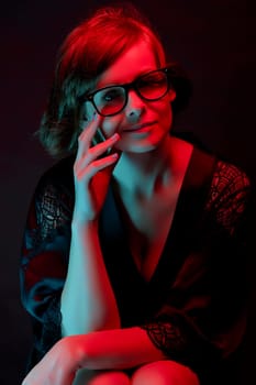 Beautiful attractive woman in glasses posing in satin bathrobe in neon light in the studio