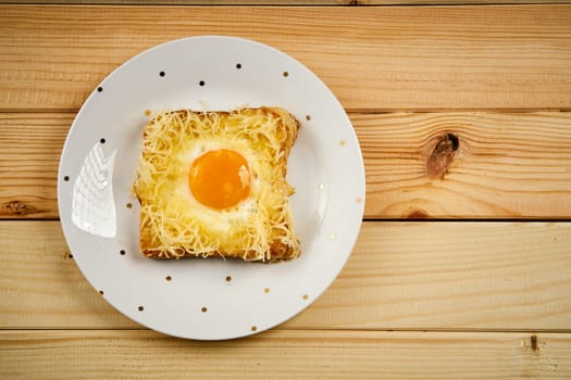 Delicious toast with fried egg on plate on bright wooden kitchen table