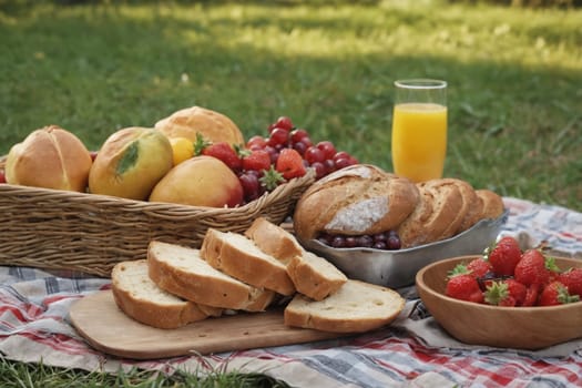 A display of tempting picnic delicacies includes two types of bread, juicy strawberries, ripe peaches, grapes, and a glass of fresh orange juice.