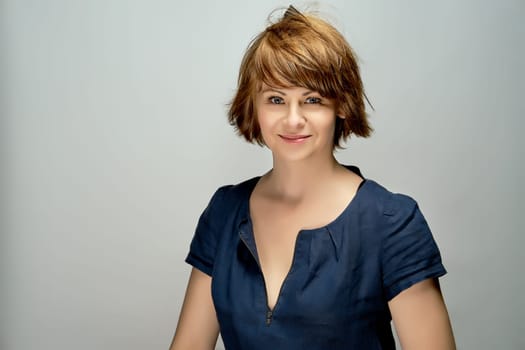 Portrait of young attractive red-haired woman in navy blue dress on gray background