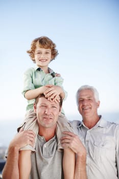 Portrait of grandfather, father and child by ocean and blue sky for bonding, relationship and relax together. Family, fun and grandpa, dad and young boy on shoulders for holiday, vacation and weekend.