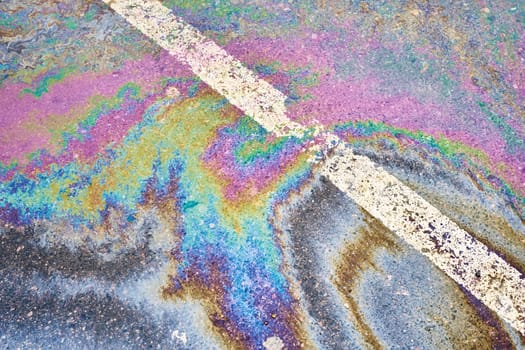 Oil discharge on rain-soaked pavement, parking lot with dividing lines, accentuating the environmental difficulties related to water pollution.