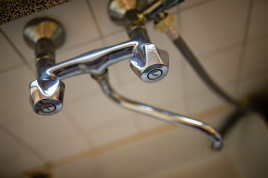 A detailed view of a modern faucet fixture in a bathroom, with visible water droplets and reflections.
