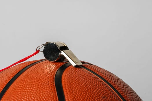 A whistle with a red lanyard is positioned carefully on top of an orange textured basketball. The neutral grey backdrop highlights the sports equipment, suggesting a pause in action during a game or practice session.