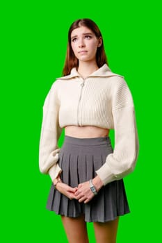 A young woman stands confidently against a vivid green background, dressed in a casual yet fashionable white cropped hoodie and a gray pleated skirt. Her expression is serene with a hint of contemplation, and her body language exudes a relaxed poise.