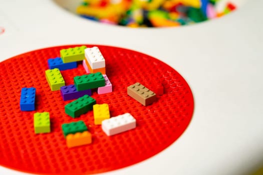 A close-up view of a childs play table filled with colorful toys. Various toys like blocks, dolls, cars, and puzzles are scattered around the table. The childs hands are seen playing and interacting with the toys.