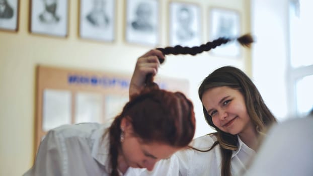 Fun schoolgirls in the classroom. Girl playing with her friend's pigtail