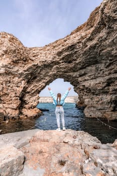 Sea woman rocks grotto. A woman in a blue jacket stands on a rock above a cliff above the sea and looks at the raging ocean. Girl traveler rests, thinks, dreams, enjoys nature