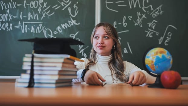 A schoolgirl wearing glasses poses against a background of books, an apple, a globe and a graduation cap