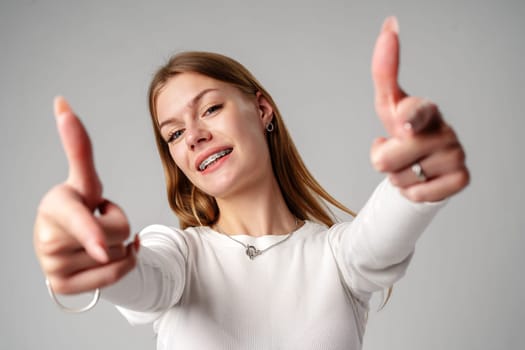 Smiling Young Woman With Braces Pointing Towards Camera in Studio close up