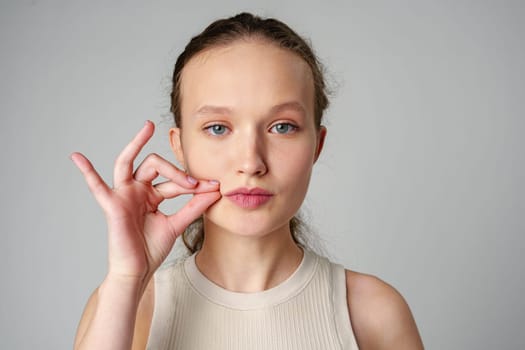 Young Woman Making a Hush Gesture on gray background in studio close up