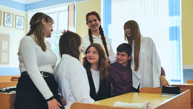 Children's education. Funny schoolchildren and their positive female teacher play fun games in creative lesson. Elementary school students laugh loudly and clap their hands together in classroom.