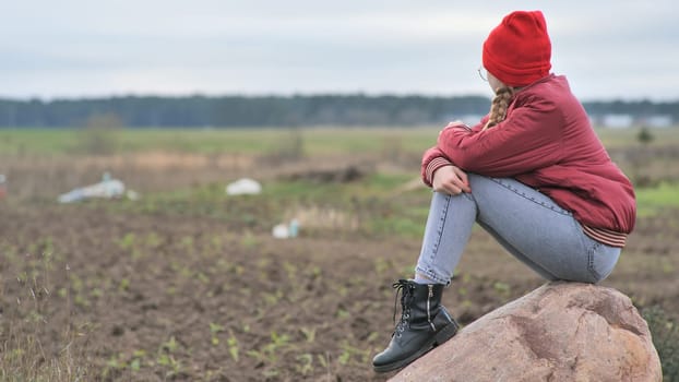 A sad teenage girl sits on a rock in a field and cries