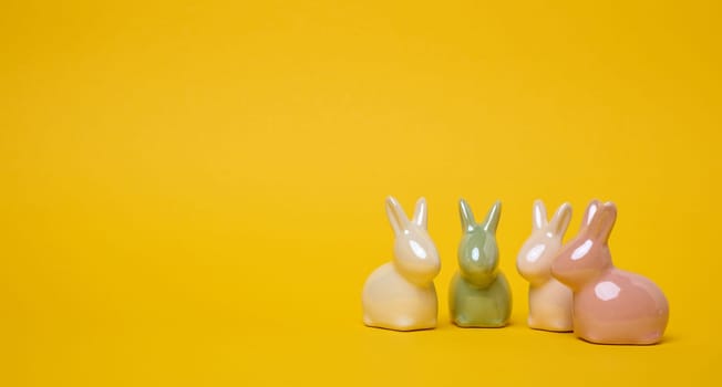 Ceramic decorative bunnies on a yellow background, festive Easter background. Copy space