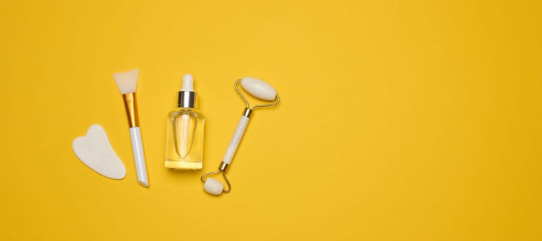 White transparent glass bottle with pipette and roller massager jade on a yellow background. Copy space