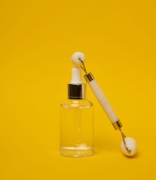 White transparent glass bottle with pipette and roller massager jade on a yellow background