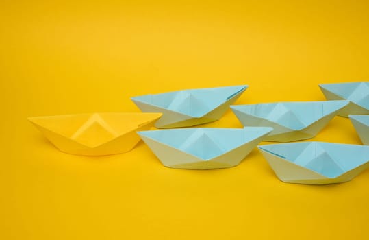 Group of blue paper boats follow yellow against a yellow background. Strong leader concept, mass manipulation. Starting a business with a well-coordinated team, start-up