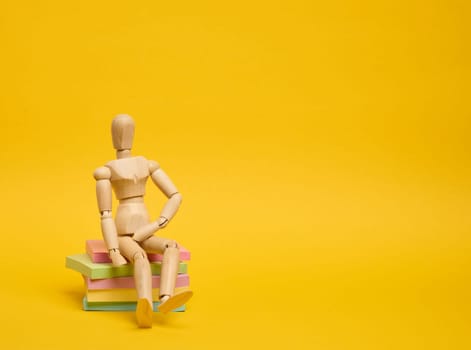 A wooden puppet doll sits on a stack of paper multi-colored stickers on a yellow background,  copy space