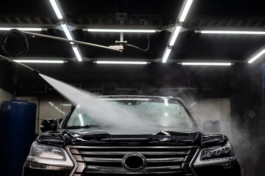 A man washes foam off a black car with water at a car wash