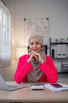 Muslim female entrepreneur wearing hijab sits working with laptop managing personal business in private office..