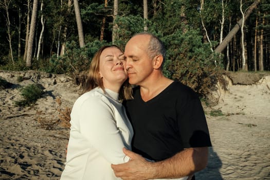 A man and a woman hug each other warmly on a sandy beach near the forest