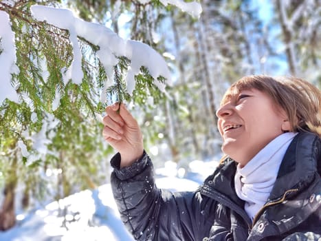 A cheerful middle aged woman in a winter coat taking selfie on nature outdoors in sunny day with blue sky