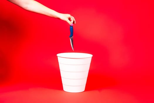 Knife is thrown into the trash basket. Red isolated background