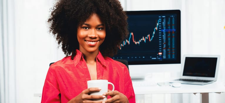 Analytical young African American businesswoman, a specialist in successful stock exchange trading, against dynamic data graph displaying marketing trend analysis on screen. Tastemaker.