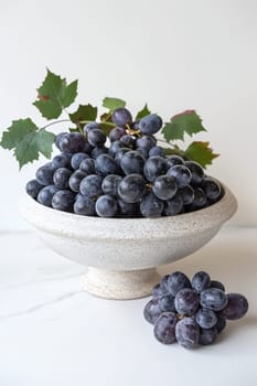 A bowl of grapes with leaves on a white table