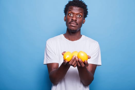 African american male individual carrying lemons and looking at the camera. Black man holding and showing yellow, citrus fruits for vitamins, nutrition, and healthy lifestyle.