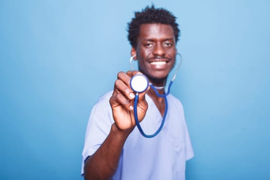 Close-up of African American healthcare specialist holding a stethoscope towards camera. Smiling black nurse in uniform grasping a medical instrument for heart or lung examination.