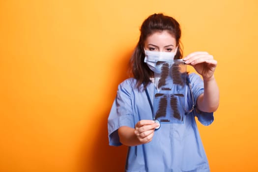 Portrait of doctor holding x-ray scan in front of the camera while wearing coronavirus mask. During covid19 epidemic, nurse practitioner examines the findings of chest radiography.