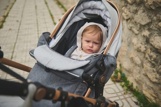 Authentic portrait of a Caucasian cute baby boy 7-9 months old in baby stroller outdoors