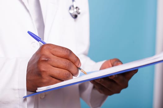 Close-up on African American pair of hands holding a pen and clipboard containing medical records. Detailed view of healthcare specialist reviewing patient charts and information.