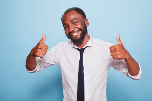 Portrait of african american man showing thumbs up sign in front of camera. Positive black individual giving like and approval, feeling happy and excited while advertising positivity.