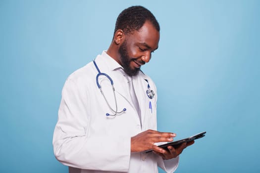 Black man wearing lab coat and stethoscope utilizing modern technology for medical research. African american doctor using digital tablet to review patients healthcare information.