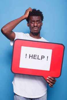 Bewildered african american individual holding voice bubble with text message asking for help. Portrait of black guy with hand on his head is grasping a red cardboard sign.