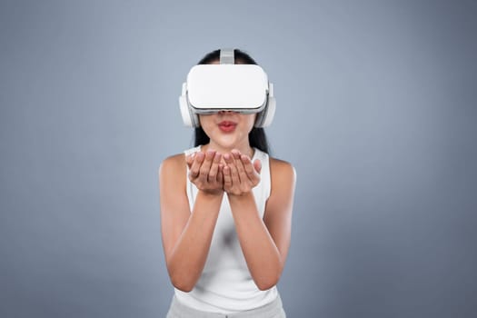 Smart female standing with gray background wearing VR headset connecting metaverse, futuristic cyberspace community technology. Elegant woman excited seeing generated virtual scenery. Hallucination.