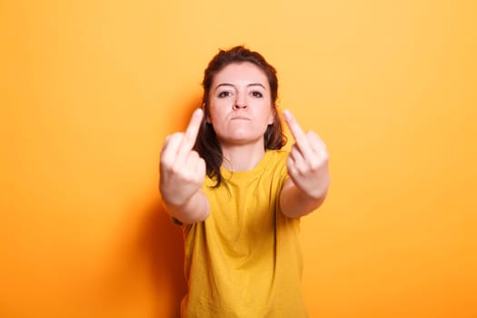 Confident brunette woman doing aggressive, vulgar hand gestures against isolated background. Portrait of caucasian female person showing middle fingers towards the camera.