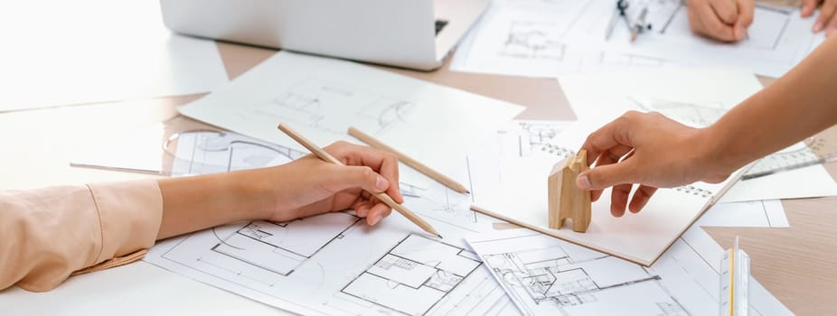 Professional architect hand draws a blueprint on table with architectural document and wooden block scatter around at office. Design and Planing concept. Focus on hand. Closeup. Delineation.