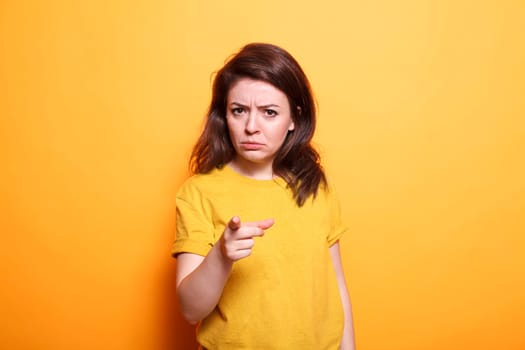 Displeased woman with serious expression points her finger at the camera. Standing over isolated background, dissatisfied person who is upset and irritated makes frustrated and angry gesture.