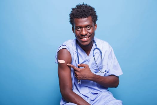 African american medical nurse having adhesive bandage after vaccination against coronavirus. Vaccinated male nurse with scrubs pointing at vaccine shot patch for immunity.