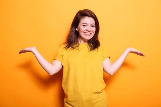 Delighted, thrilled woman with extended arms, brown hair, and a big smile stands against isolated orange background. She exudes happiness and contentment and radiates positive emotions.