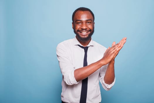 Smiling male adult clapping hands and cheering on job well done, enjoying a significant win. Excited black man expressing his congratulations with an applause gesture and positive response.
