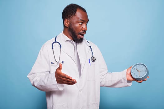 African American general practitioner shockingly looking at clock before a patient medical consultation. Black doctor appears to be in a panic, rushing and experiencing a healthcare emergency.