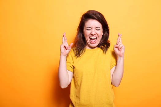 Young beautiful brunette woman casually dressed over isolated background having fingers crossed and hopefully smiling with eyes closed. Caucasian lady is excited about winning.