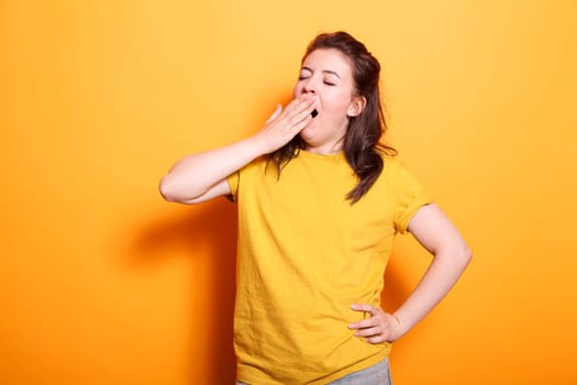 Portrait of caucasian woman yawning and covering her mouth, feeling sleepy in studio. Tired female person falling asleep while posing and standing over isolated background.