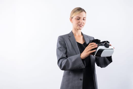 Caucasian business woman holding VR glass while standing at white background. Professional project manager looking visual reality goggle while wearing suit. Innovation technology concept. Contraption.