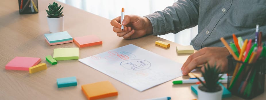 Skilled businessman brainstorms marketing ideas using mind maps. Successful male startup leader drafts financial plan on table with sticky notes scatter around. Closeup. Focus on hand.Variegated.