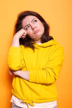 Caucasian woman with a sharp imagination and questions in mind. Female person wearing a sweater has contemplative expression on camera, hand resting on forehead, thinking about an idea.